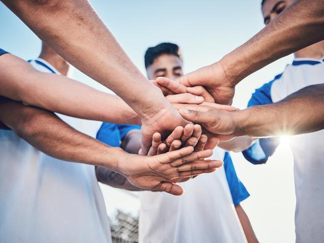 Fünf Hände von Fußballspielern legen sich in der Mitte zusammen, symbolisieren Teamgeist und Zusammenhalt.