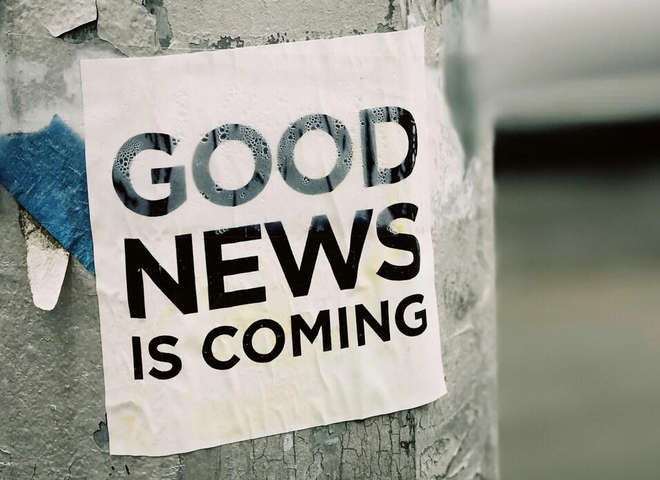 Plakat mit der Aufschrift „GOOD NEWS IS COMING“ auf einem grauen Laternenpfahl.